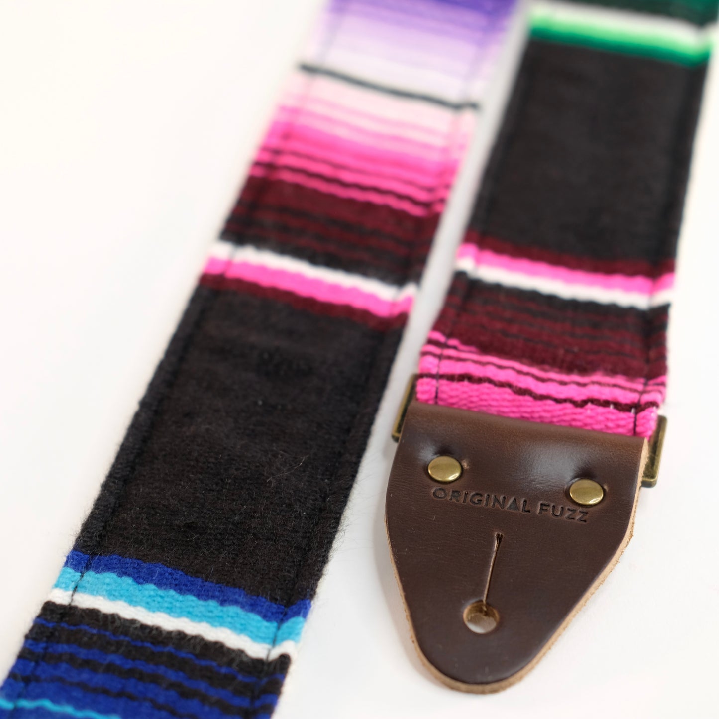 End-tab detail view of guitar strap in black serape fabric with brown leather end-tab. Made in Nashville by Original Fuzz.