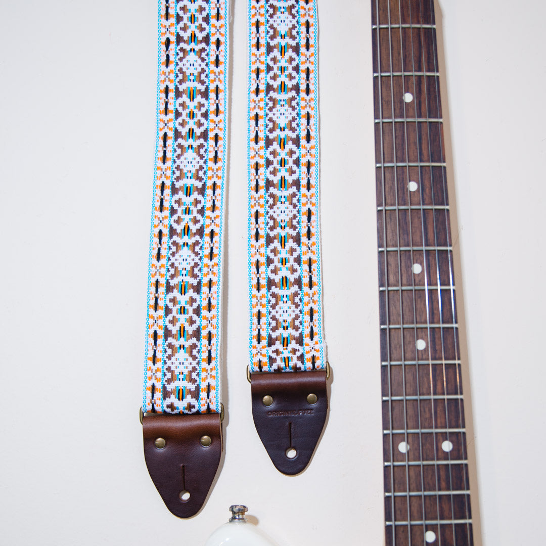 Detail of the vintage guitar strap in Merrimon Ave next to the fretboard of an electric guitar