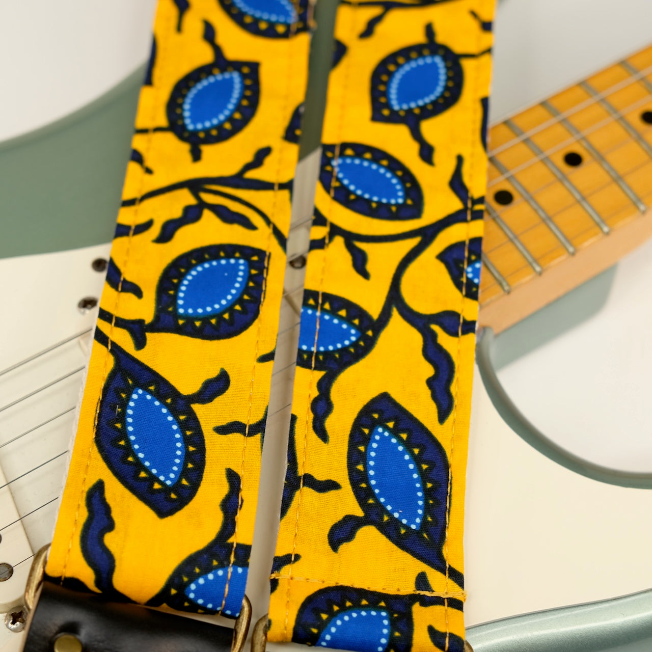 Wide view of guitar strap in yellow and blue botanical African wax print fabric with black leather end-tab. Made in Nashville by Original Fuzz.