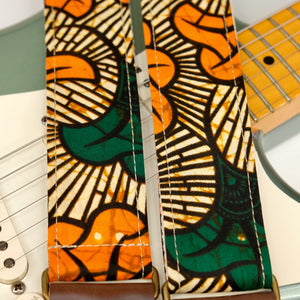 Wide view of guitar strap in tan, orange, and green botanical African wax print fabric with brown leather end-tab. Made in Nashville by Original Fuzz.