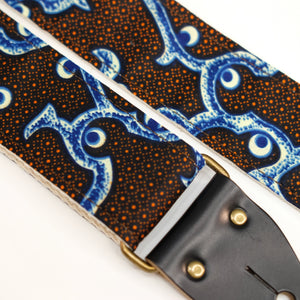 Fabric detail view of guitar strap in black, blue, cream, and orange botanical African wax print fabric with black leather end-tab. Made in Nashville by Original Fuzz.