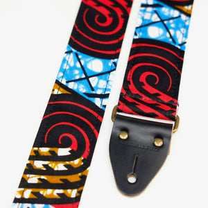 End-tab detail view of guitar strap in black, red, blue, and tan swirled African wax print fabric with black leather end-tab. Made in Nashville by Original Fuzz.