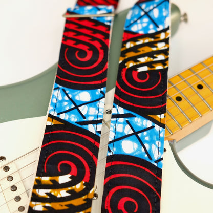 Wide view of guitar strap in black, red, blue, and tan swirled African wax print fabric with black leather end-tab. Made in Nashville by Original Fuzz.