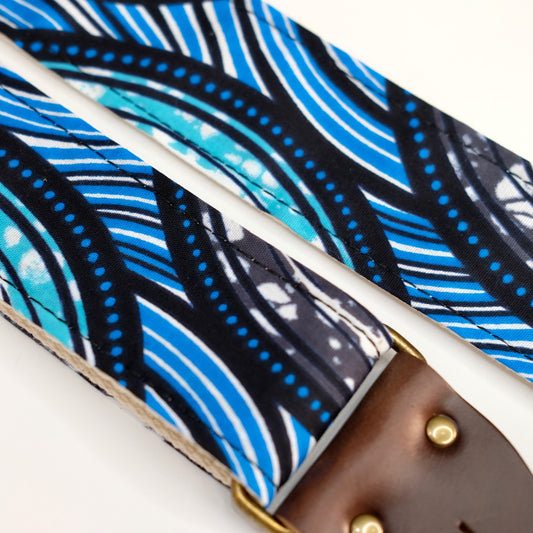 Fabric detail view of guitar strap in teal, gray, white, black, and blue rippled African wax print fabric with brown leather end-tab. Made in Nashville by Original Fuzz.