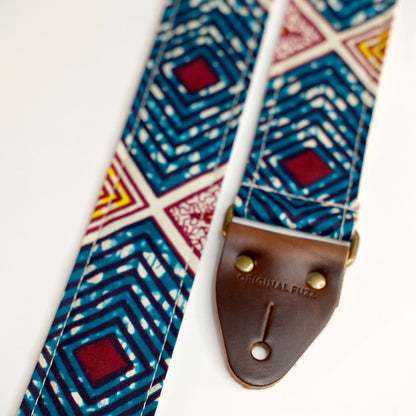 End-tab detail view of guitar strap in dark teal, burgundy, cream, and yellow diamond tile African wax print fabric with brown leather end-tab. Made in Nashville by Original Fuzz.