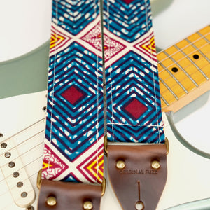Wide view of guitar strap in dark teal, burgundy, cream, and yellow diamond tile African wax print fabric with brown leather end-tab. Made in Nashville by Original Fuzz.