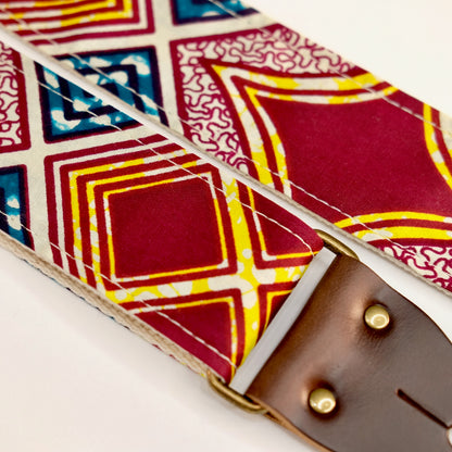 Fabric detail view of guitar strap in burgundy, cream, yellow, and dark teal diamond tile African wax print fabric with brown leather end-tab. Made in Nashville by Original Fuzz.