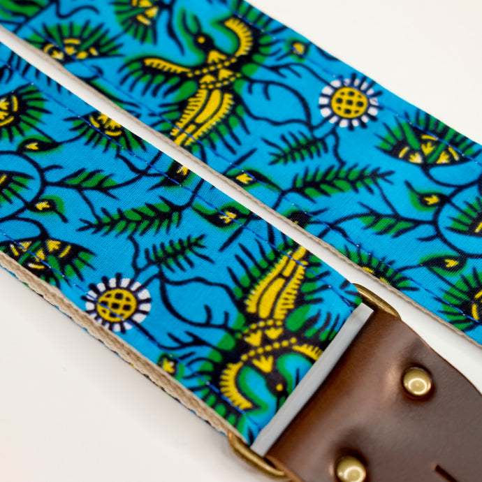Fabric detail view of guitar strap in blue, yellow, and green botanical African wax print fabric with brown leather end-tab. Made in Nashville by Original Fuzz.