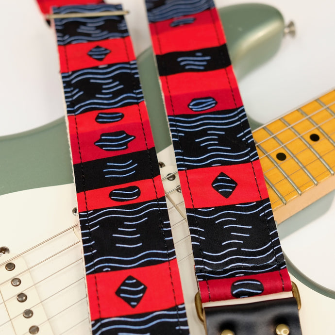 Wide view of guitar strap in black, red, and white striped African wax print fabric with black leather end-tab. Made in Nashville by Original Fuzz.