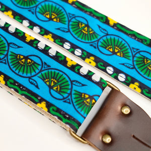 Fabric detail view of guitar strap in blue, yellow, and green bordered botanical African wax print fabric with brown leather end-tab. Made in Nashville by Original Fuzz.