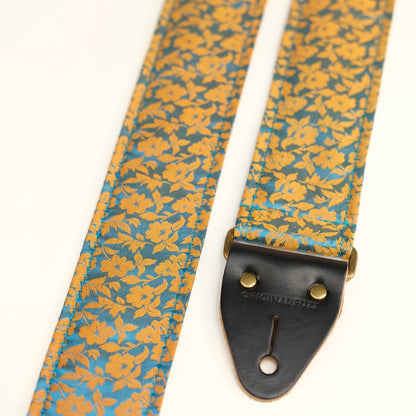 End-tab detail view of guitar strap in mustard yellow and teal silk floral fabric with black leather end-tab. Made in Nashville by Original Fuzz.