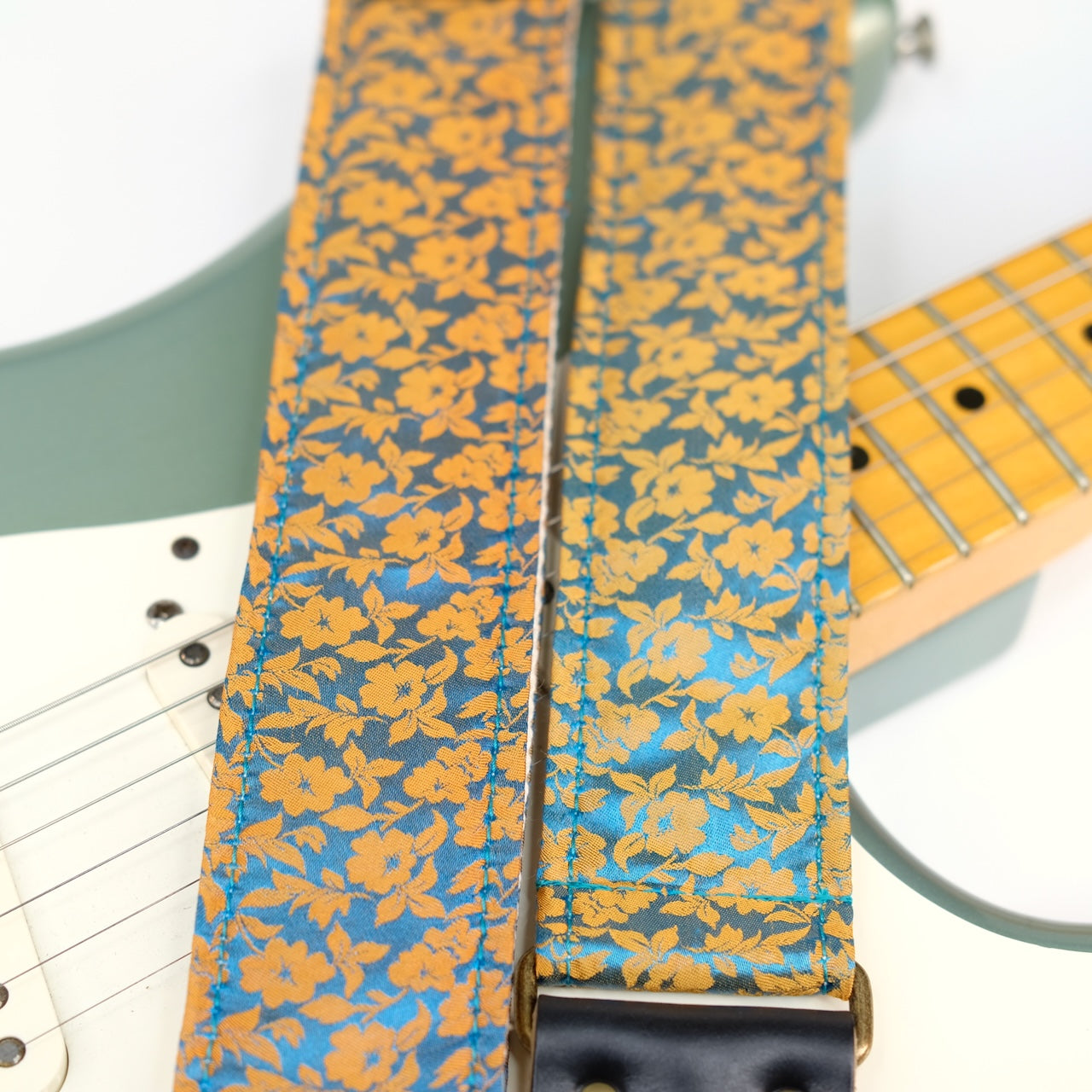 Wide view of guitar strap in mustard yellow and teal silk floral fabric with black leather end-tab. Made in Nashville by Original Fuzz.