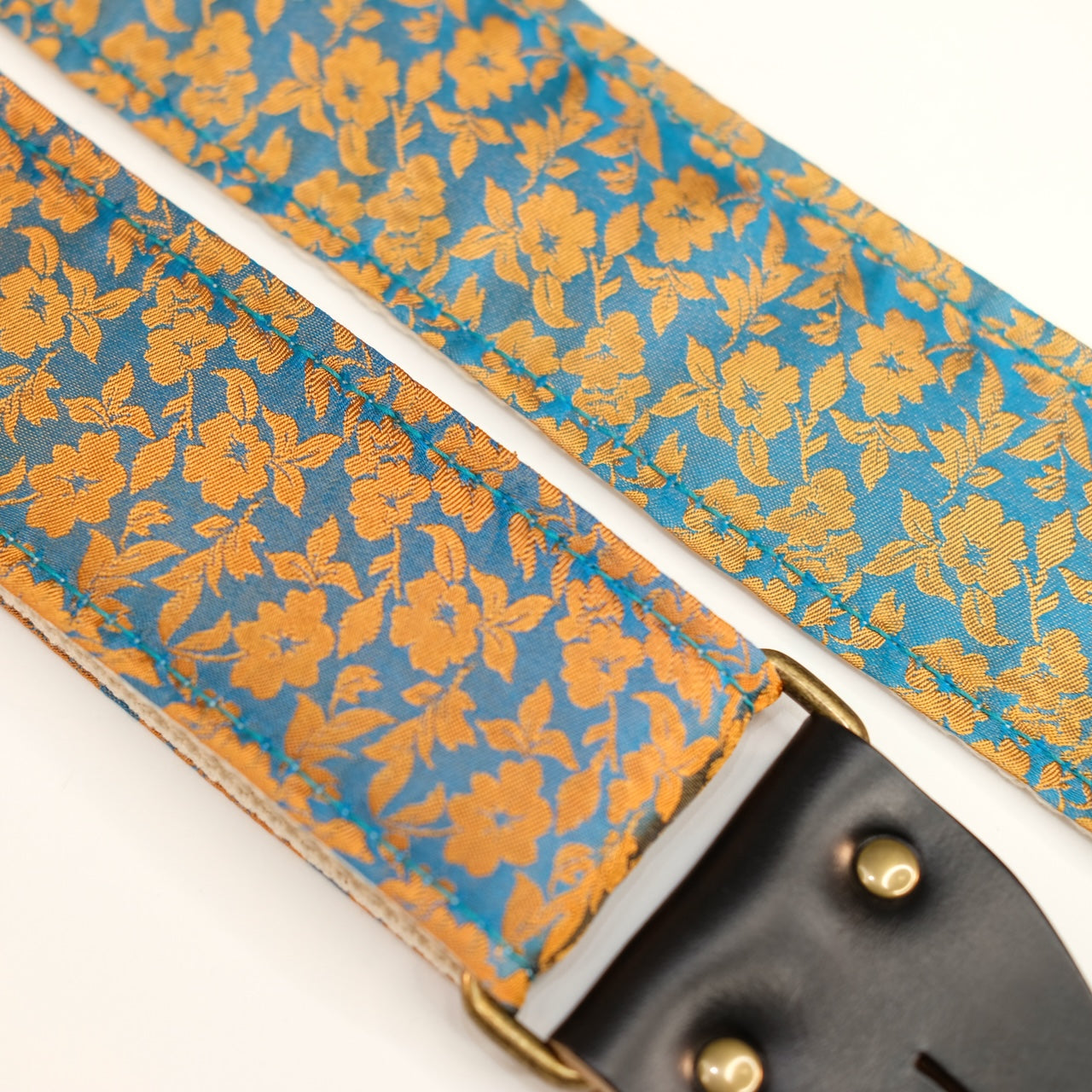 Fabric detail view of guitar strap in mustard yellow and teal silk floral fabric with black leather end-tab. Made in Nashville by Original Fuzz.