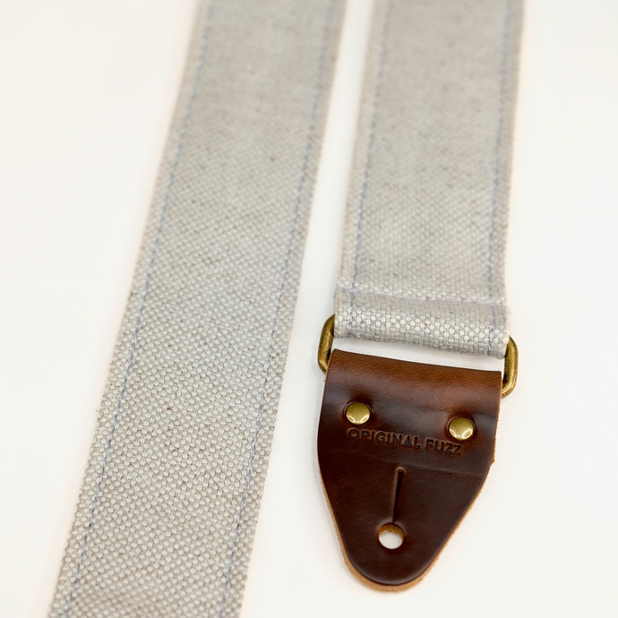 End-tab detail view of guitar strap in pale blue-grey woven fabric with brown leather end-tab. Made in Nashville by Original Fuzz.