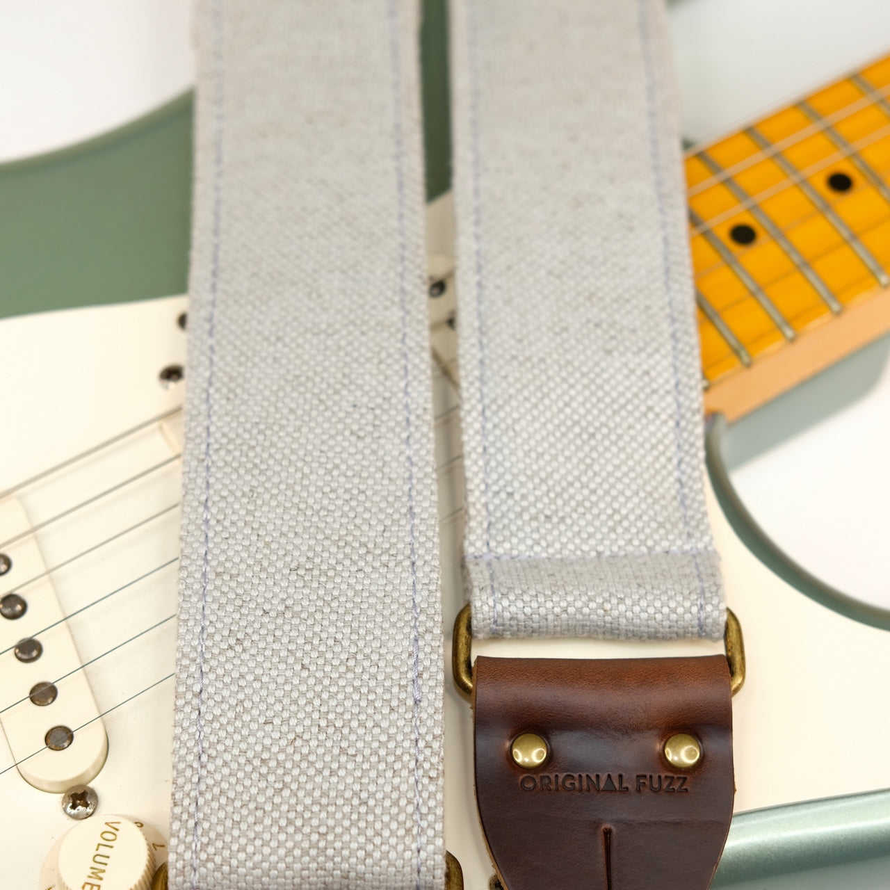 Wide view of guitar strap in pale blue-grey woven fabric with brown leather end-tab. Made in Nashville by Original Fuzz.