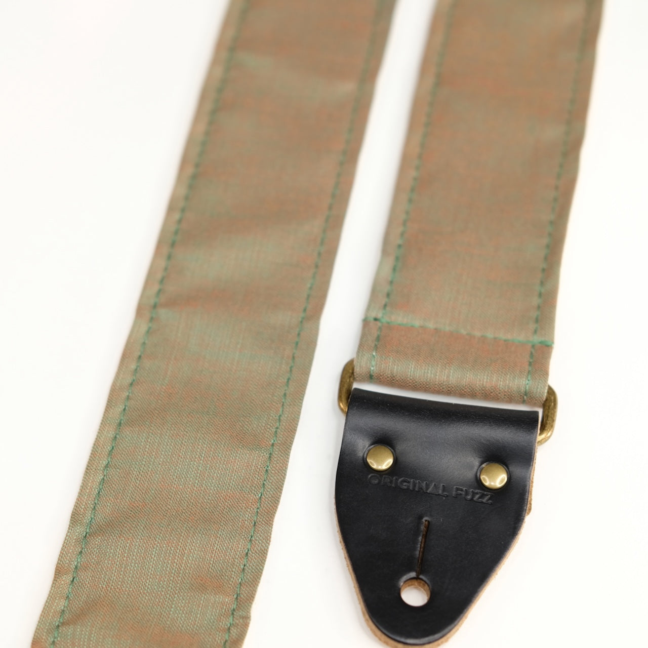 End-tab detail view of guitar strap in green-brown silky woven fabric with black leather end-tab. Made in Nashville by Original Fuzz.