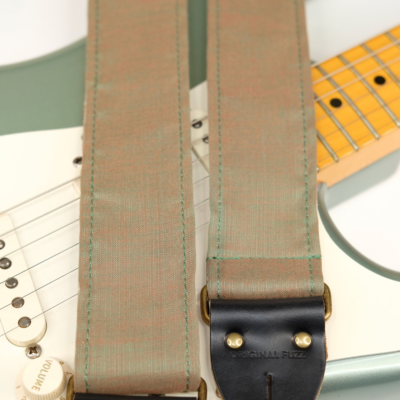 Wide view of guitar strap in green-brown silky woven fabric with black leather end-tab. Made in Nashville by Original Fuzz.