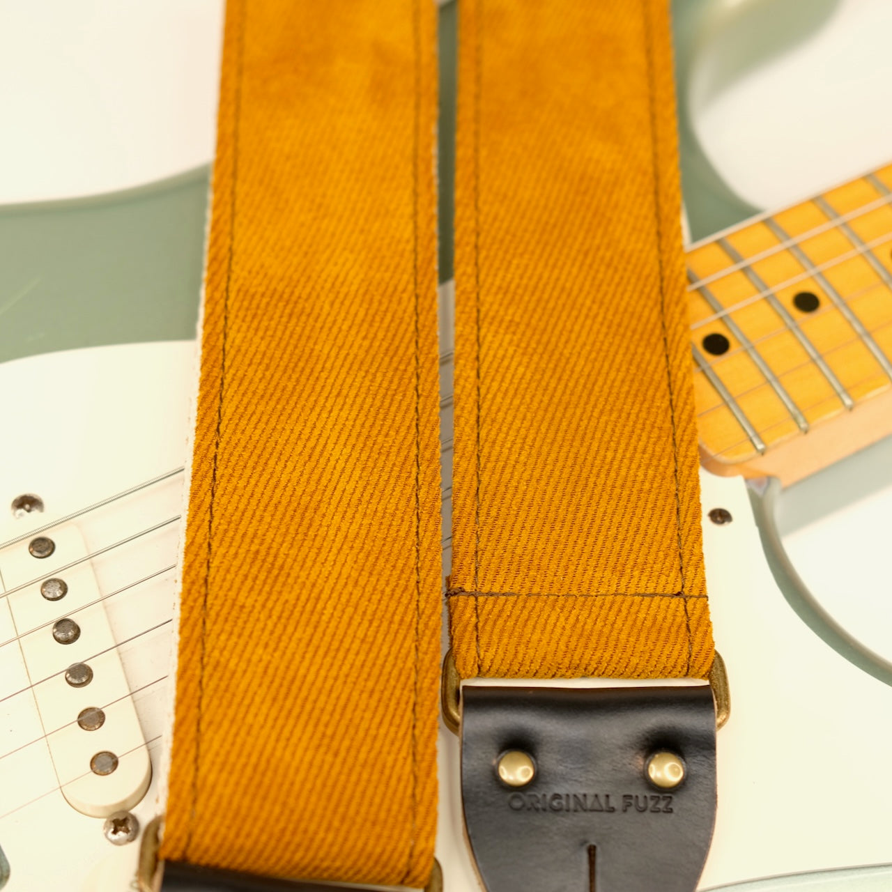 Wide view of guitar strap in golden brown woven fabric with black leather end-tab. Made in Nashville by Original Fuzz.