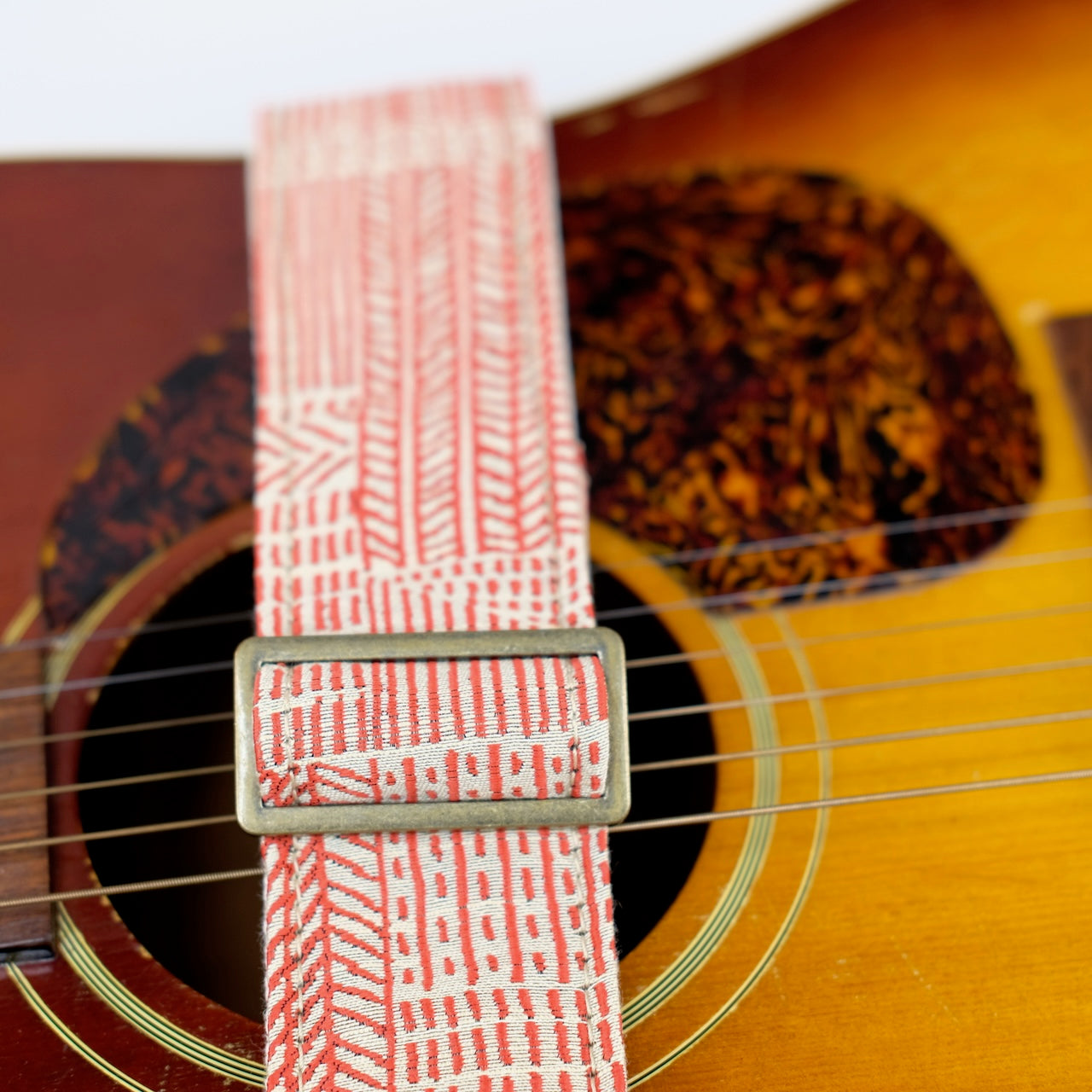 Buckle detail of guitar strap in beige and red line art woven fabric with brown leather end-tab. Made in Nashville by Original Fuzz.