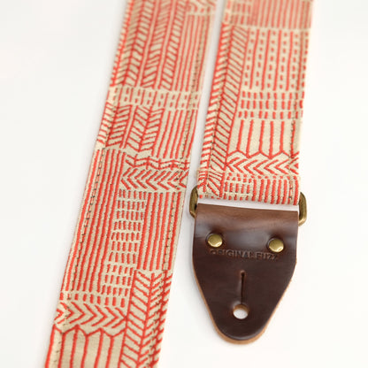 End-tab detail view of guitar strap in beige and red line art woven fabric with brown leather end-tab. Made in Nashville by Original Fuzz.