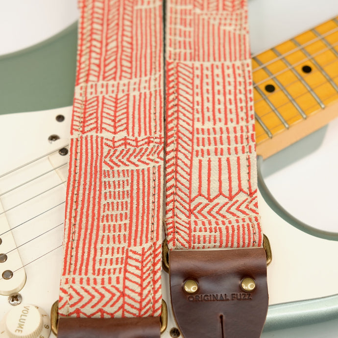Wide view of guitar strap in beige and red line art woven fabric with brown leather end-tab. Made in Nashville by Original Fuzz.
