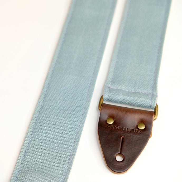 End-tab detail view of guitar strap in light blue woven fabric with brown leather end-tab. Made in Nashville by Original Fuzz.