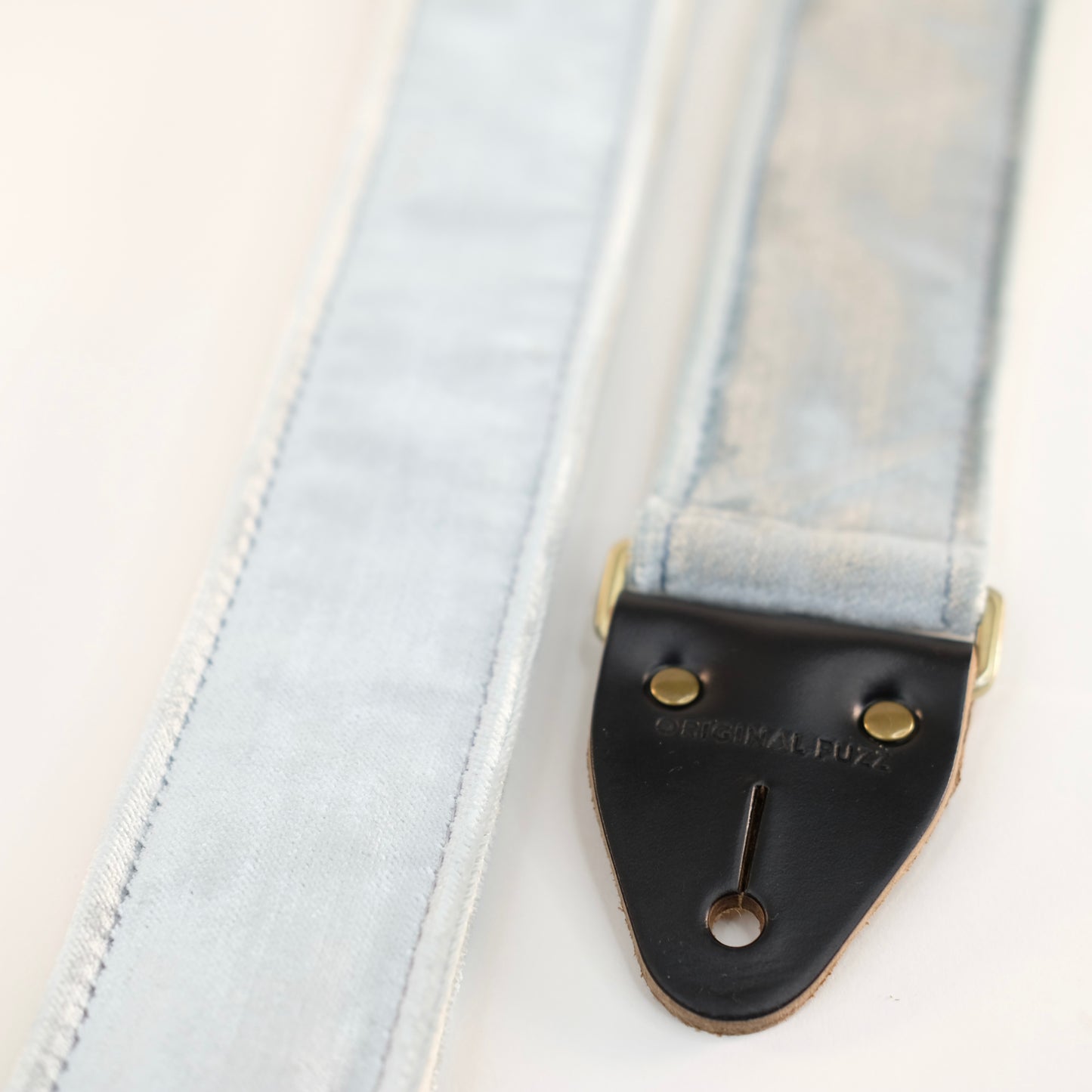 End-tab detail view of guitar strap in pale silver blue velvet with black leather end-tab. Made in Nashville by Original Fuzz.