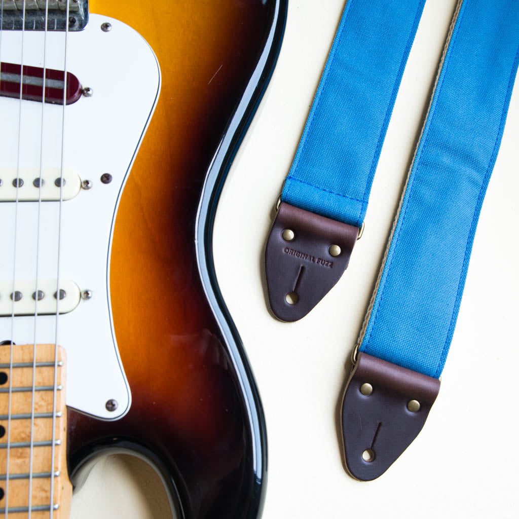 Blue vintage-style cotton canvas guitar strap with antique brass hardware made by Original Fuzz in Nashville with a Fender Jazzmaster.