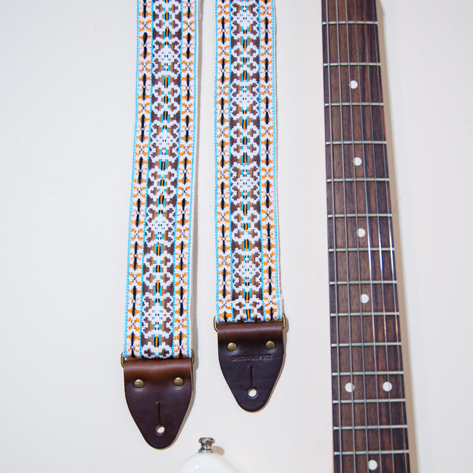 Detail of the vintage guitar strap in Merrimon Ave next to the fretboard of an electric guitar